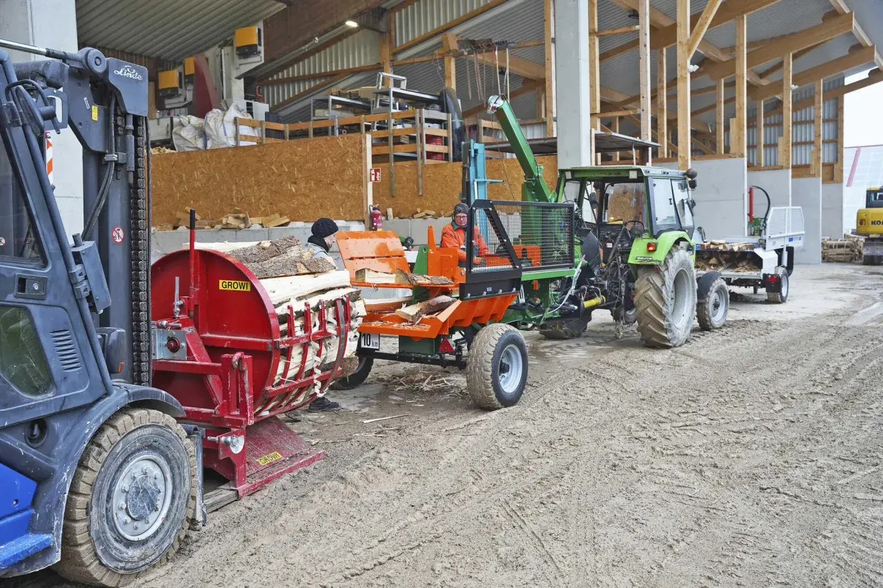 Holzspalter und Traktor mit Anhänger, bereit für den Transport. Die mobilen Förderbänder sind im Einsatz, um das Holz zu bewegen.
