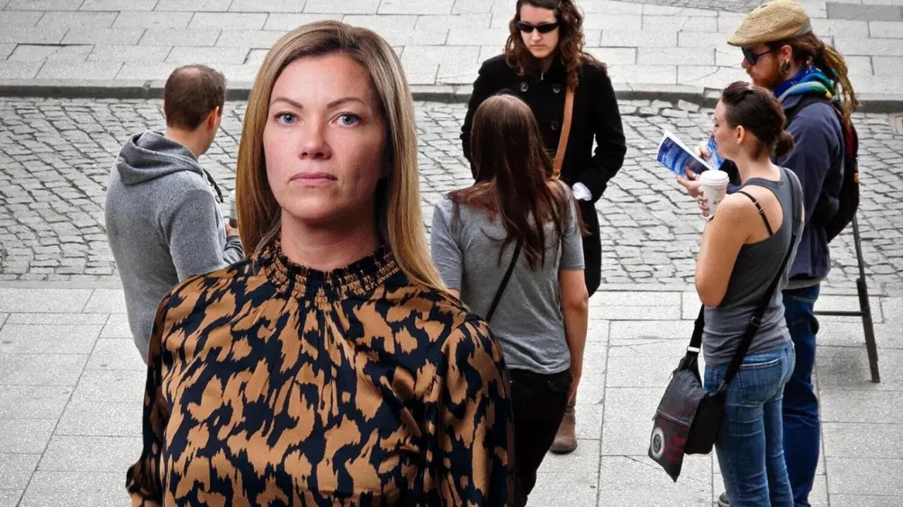 En kvinna med en mönstrad blus tittar framåt. I bakgrunden syns flera personer, en del verkar diskutera, vilket kan symbolisera ansvarstagande på jobbet.