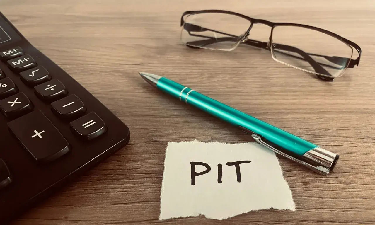 Kalkulator, zielony długopis i okulary leżą obok kartki z napisem PIT. Czas rozliczyć PIT 36L.