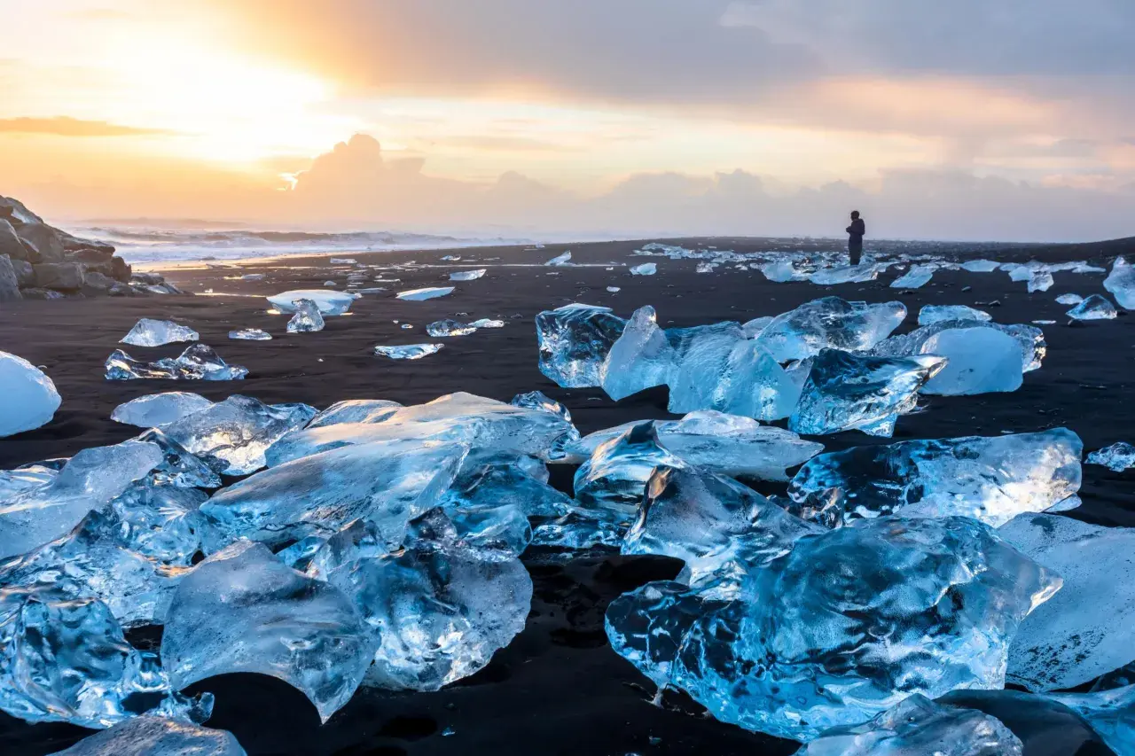 Fragmentos de hielo brillan en la arena negra del Diamond Beach de Islandia, bajo un cielo crepuscular.