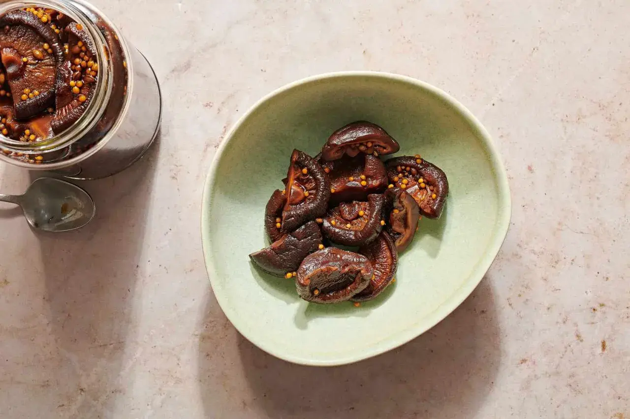 A jar and bowl of glistening pickled shiitake mushrooms, studded with mustard seeds.