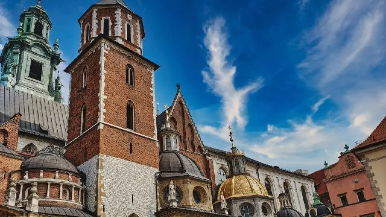 Kraków: Wawel z ceglaną wieżą, złotą kopułą i zielonym dachem pod błękitnym niebem.
