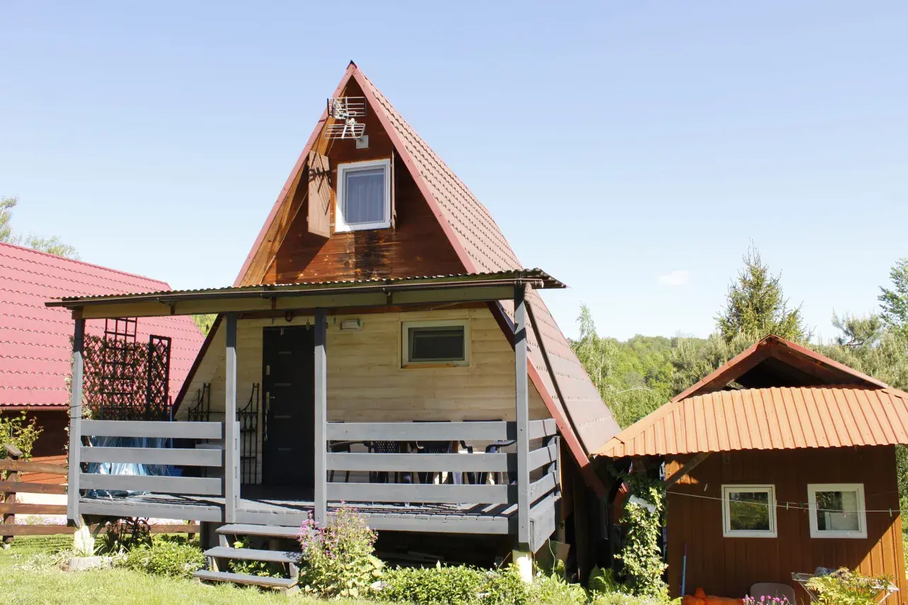Drewniany olchowiec nad Soliną, z czerwonym dachem i werandą, otoczony zielenią.