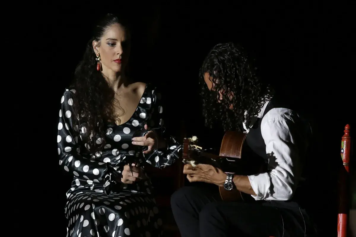 Unos buenos días flamencos con una bailaora y un guitarrista en un escenario oscuro.