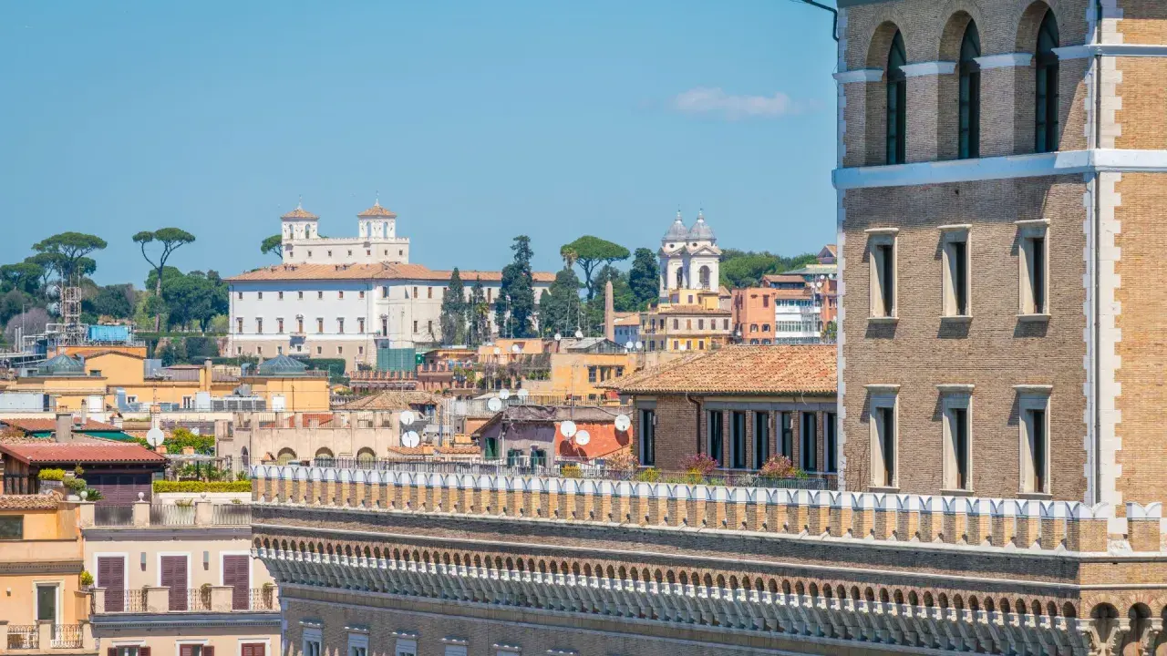 Vue panoramique de Rome, avec la Villa Médicis et ses jardins en arrière-plan, sous un ciel bleu clair.
