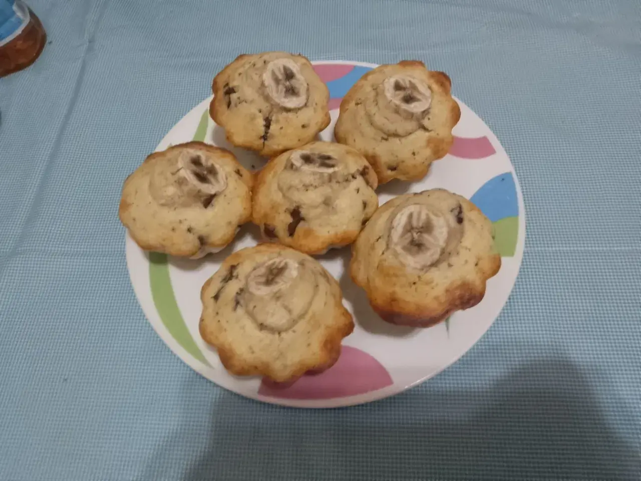 Sei muffin banana e cioccolato, guarniti con una fetta di banana, su un piatto colorato.