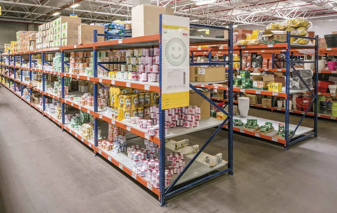 Wnętrze magazynu typu dark store z rzędami regałów wypełnionych produktami spożywczymi i innymi towarami.