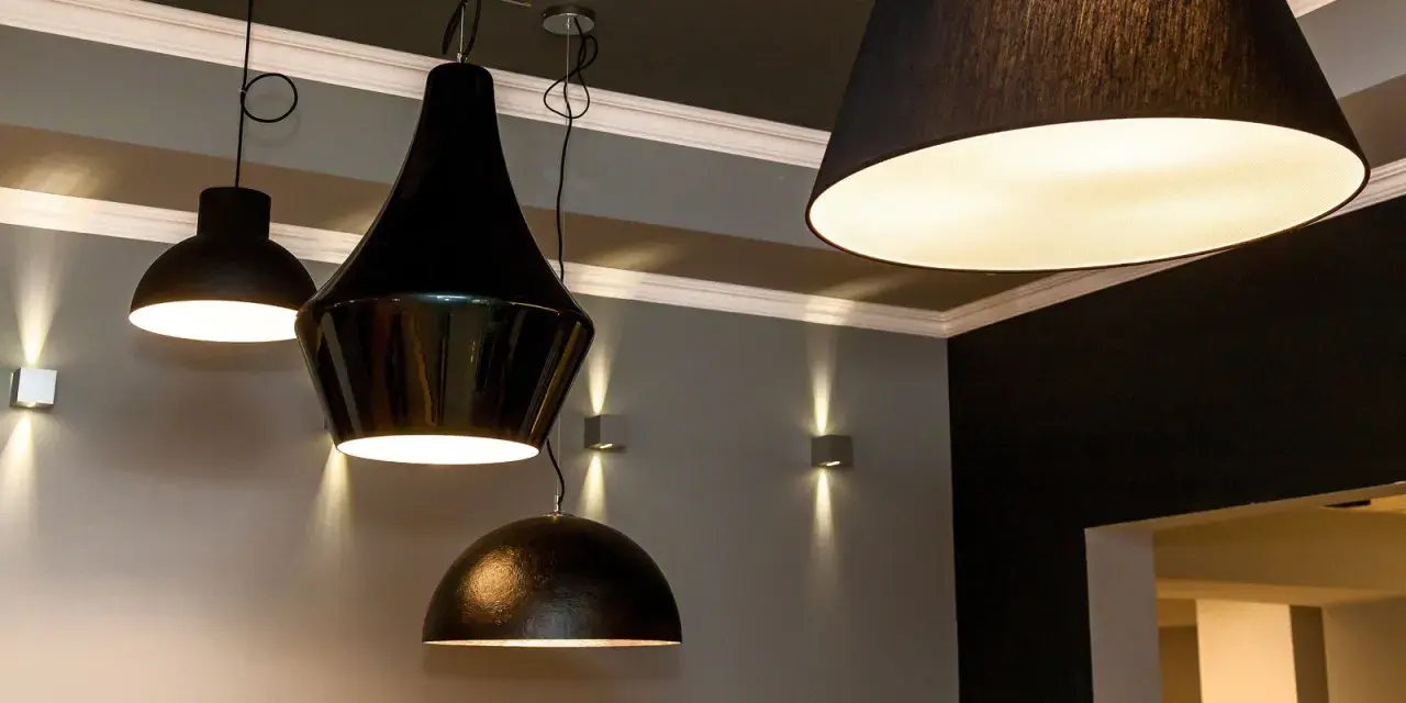 Variedad de lámparas colgantes y apliques de pared en negro y dorado, iluminando un espacio moderno.