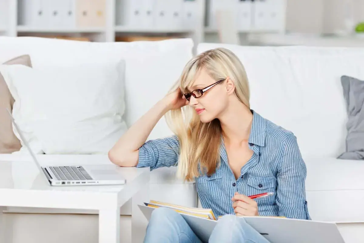 Junge Frau lernt am Laptop, ideal für online studium kostenlos. Sie sitzt auf dem Boden mit Büchern und Stift.