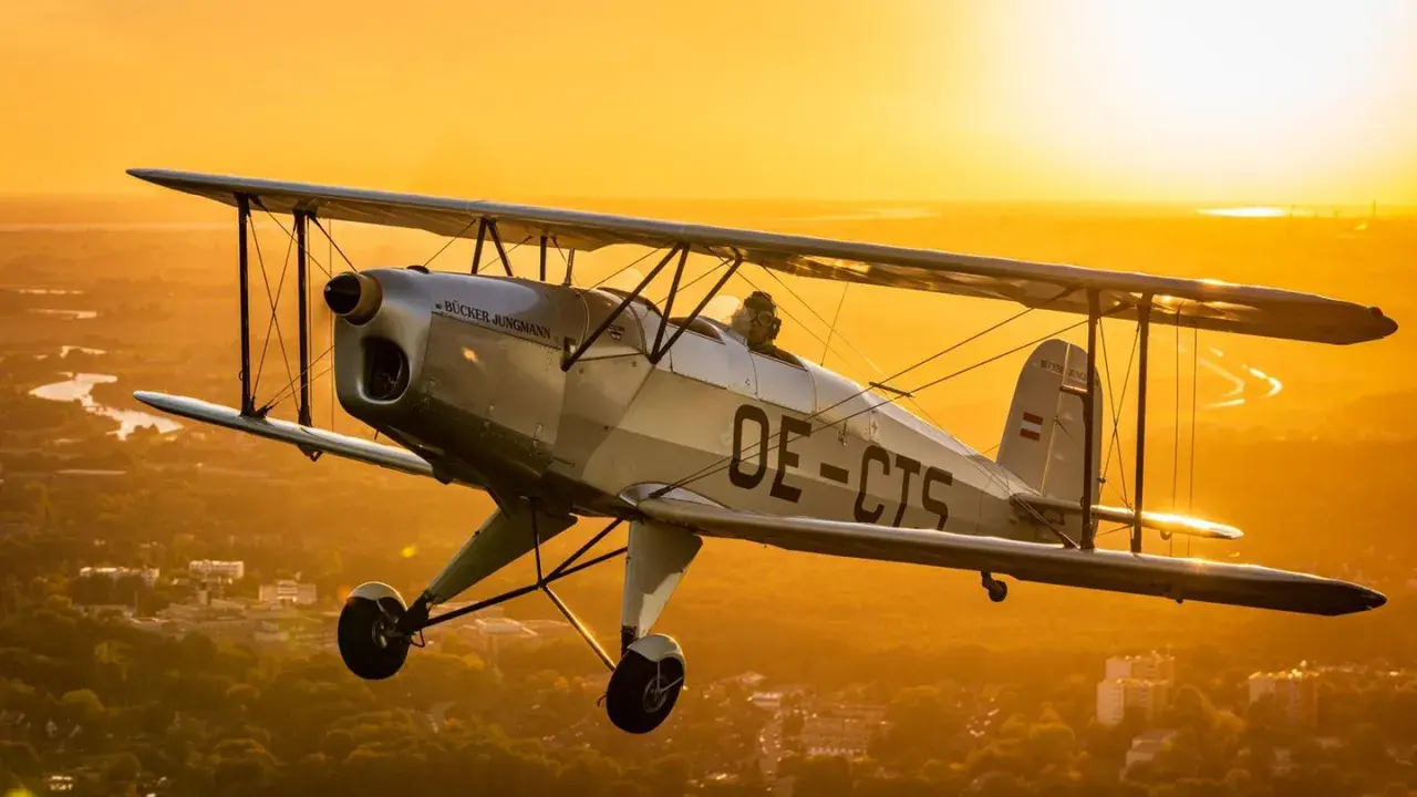 Ein silberner Doppeldecker fliegt im goldenen Abendlicht über einer Stadt. Ein Traum für alle, die gerne flugzeuge fotografieren.