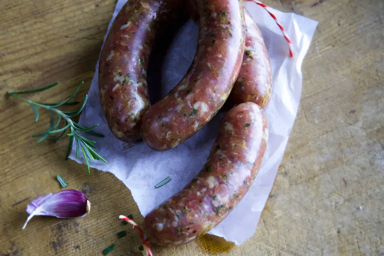 Frische italienische Bratwurst Salsiccia, bereit für ein köstliches Rezept. Rosmarin und Knoblauch liegen daneben.