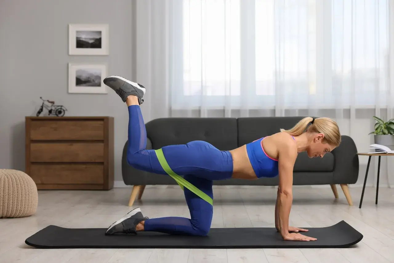 Donna con gambe toniche esegue un esercizio con elastico per glutei e gambe, in posizione quadrupedica su un tappetino.