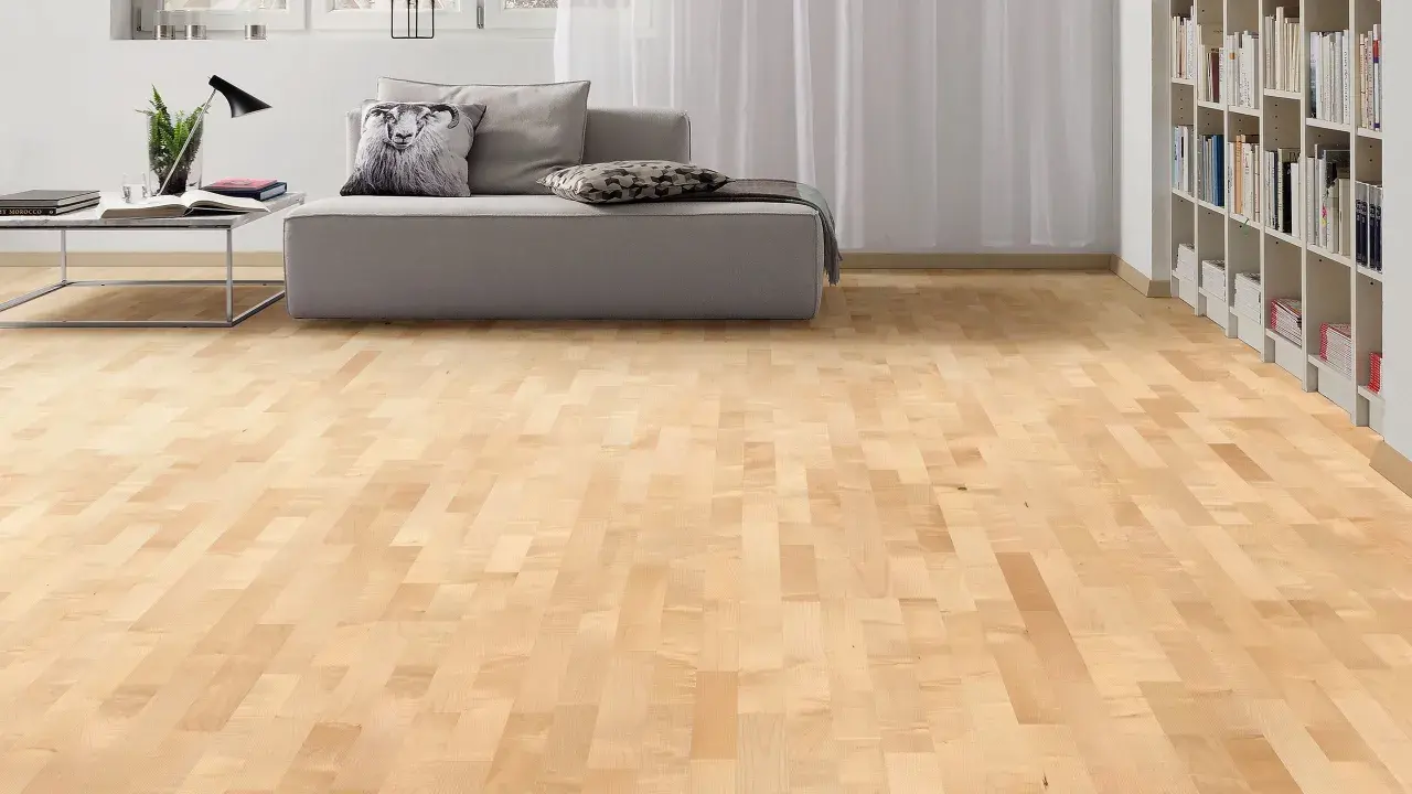 Suelo de parquet en color madera arce, con un sofá gris y estanterías llenas de libros al fondo.