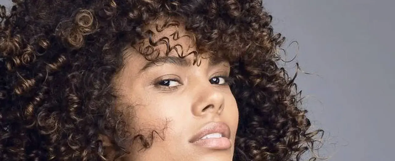 Mujer con cabello rizado y oscuro, mostrando cómo nutrir el pelo para un brillo saludable.