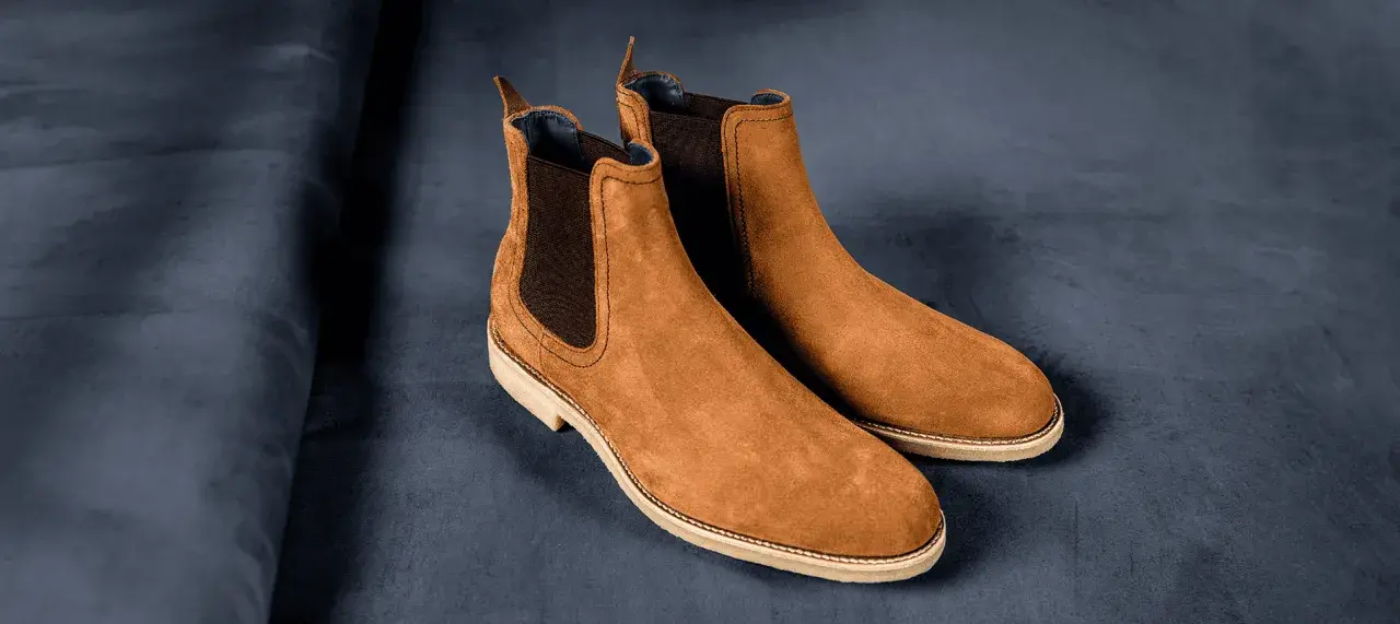 Paire de bottines Chelsea en daim marron, sur fond bleu nuit. La matière daim offre une texture douce et luxueuse.