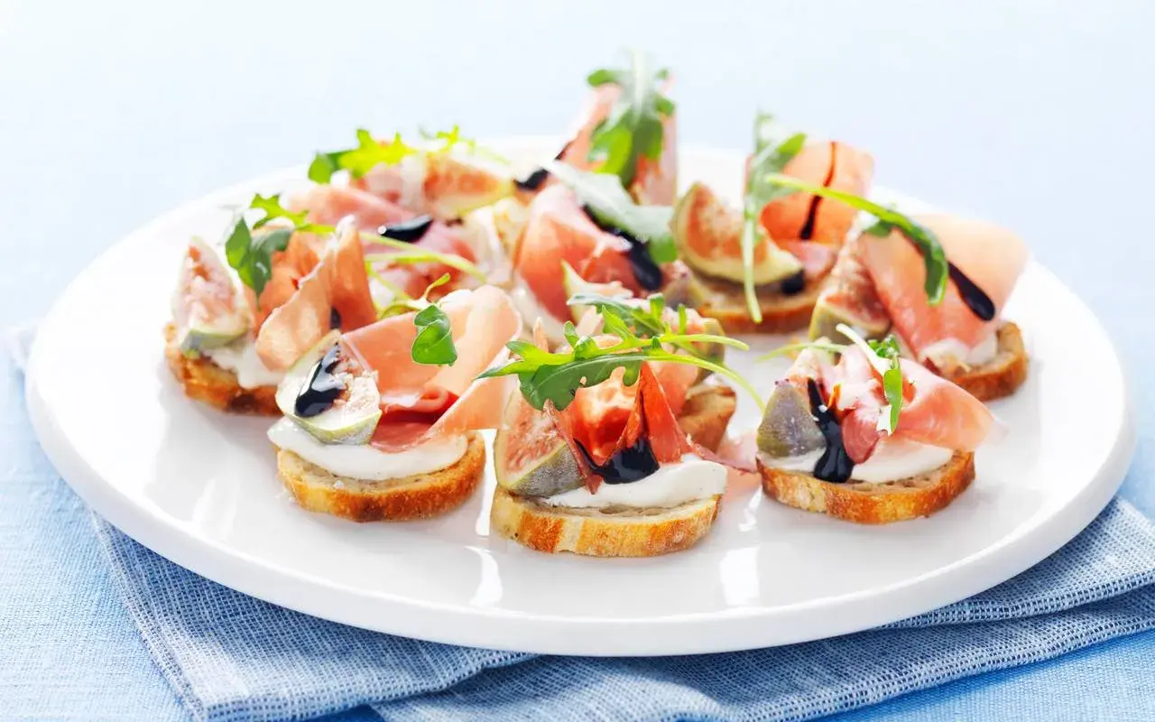 En tallrik med läckra crostini med lufttorkad skinka, färska fikon, krämig ost och ruccola, ringlad med balsamvinäger.