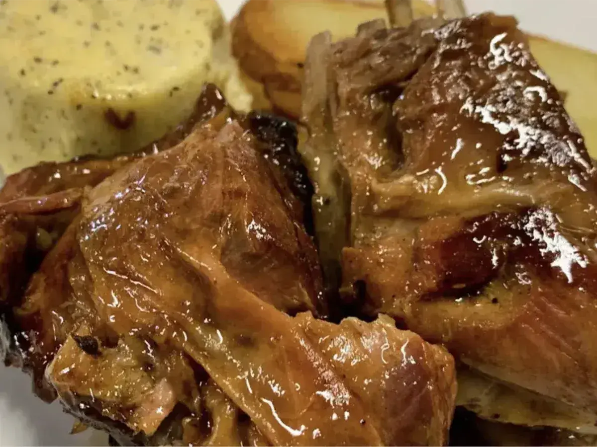 Succulento agnello al forno, dorato e lucido, servito con patate arrosto e una cremosa salsa verde.