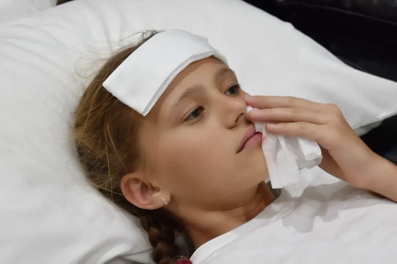 Bambina con impacco sulla fronte e fazzoletto per fermare il sangue dal naso.
