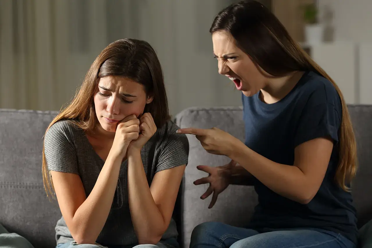 Una sorella urla e punta il dito contro l'altra, che piange. Litigi tra sorelle adulte.