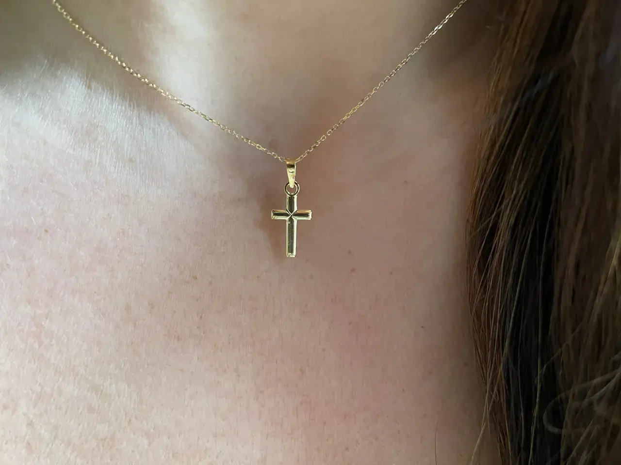 Una delicada cadena de oro sostiene una cruz de oro pequeña, un símbolo de fe y elegancia.