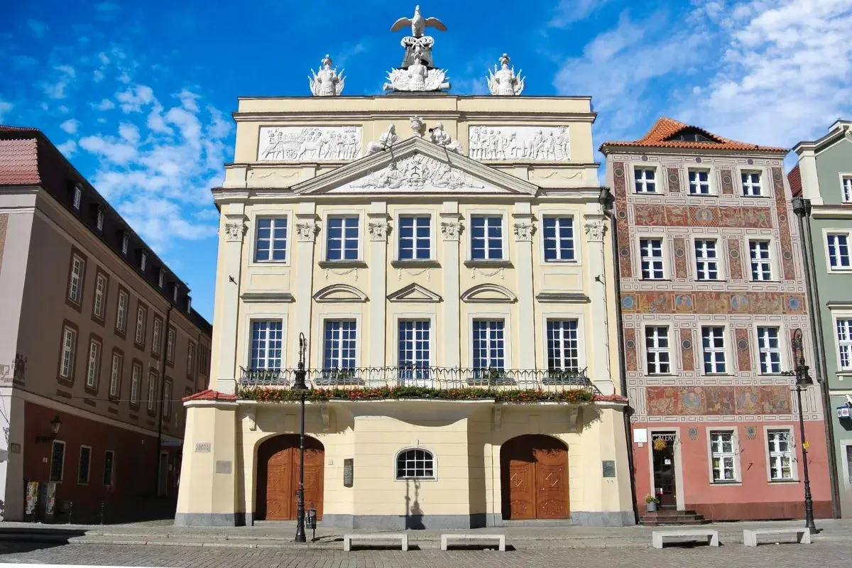 Pałac Działyńskich w Poznaniu, z bogatymi zdobieniami i orłem na szczycie, dumnie prezentuje się na tle błękitnego nieba.