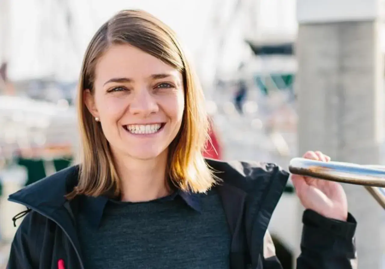 Uśmiechnięta Jessica Watson, która przetrwała sztorm, na tle łodzi.