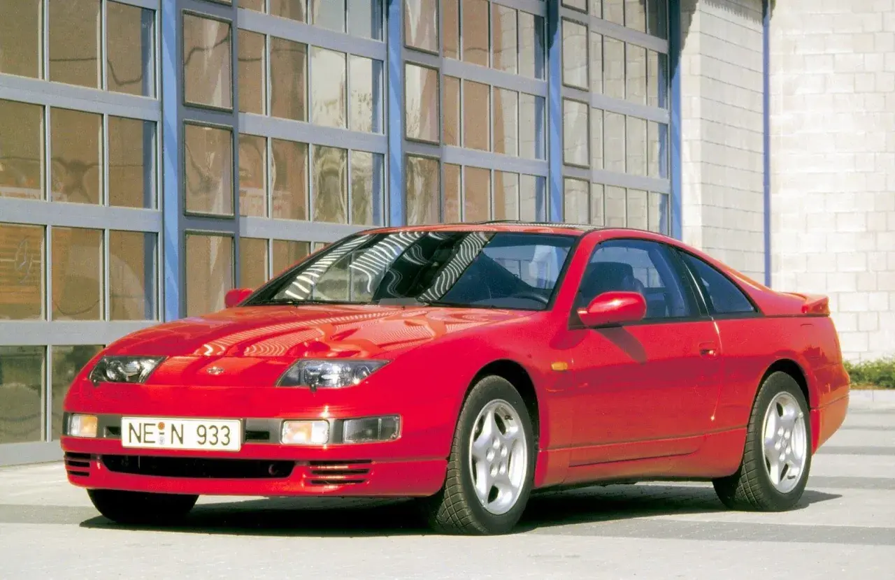 Czerwony Nissan 300zx z lat 90. stoi przed budynkiem z dużymi, przeszklonymi drzwiami.