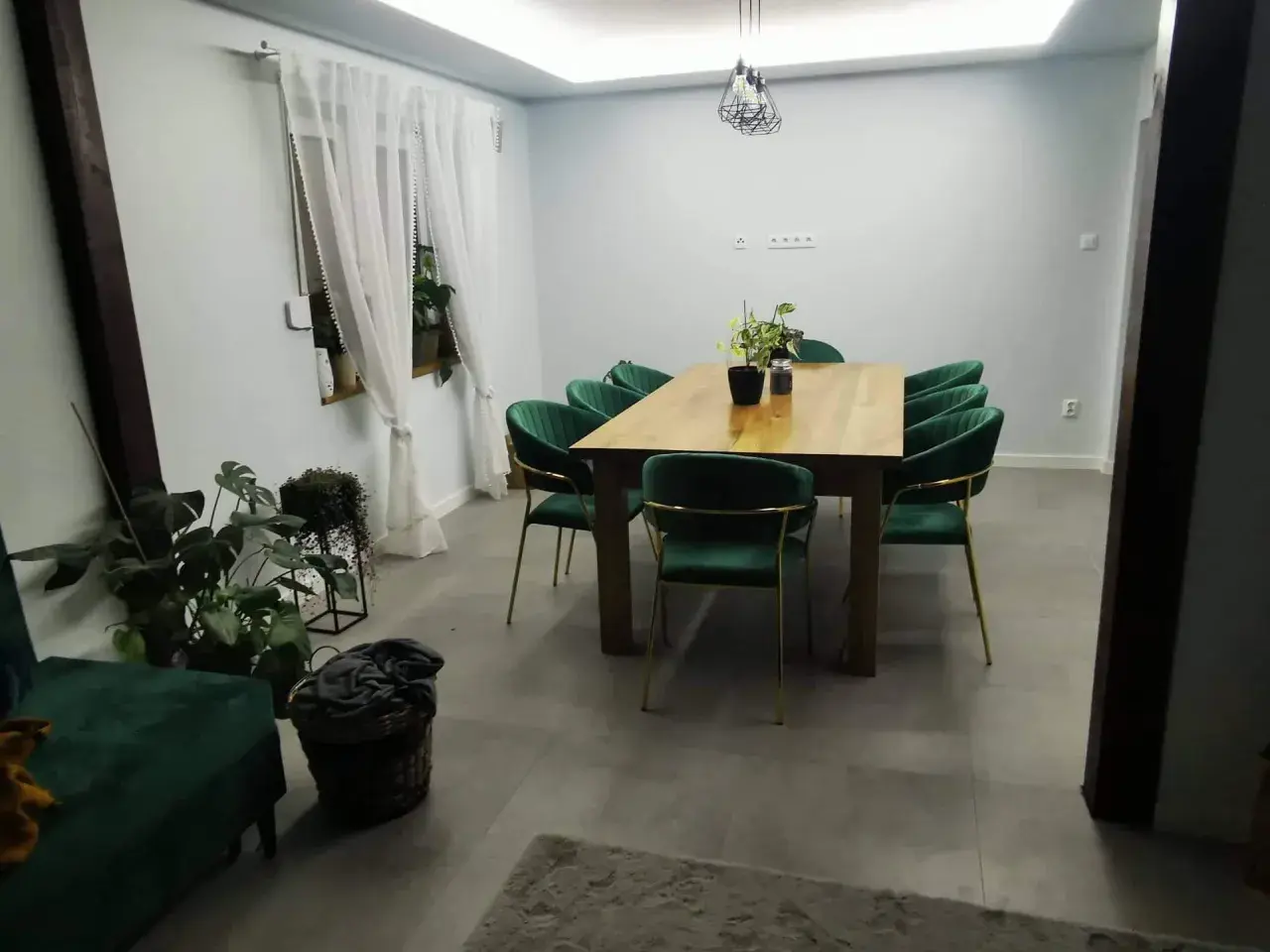 Elegancki salon w stylu glamour z zielonymi aksamitnymi krzesłami i drewnianym stołem.
