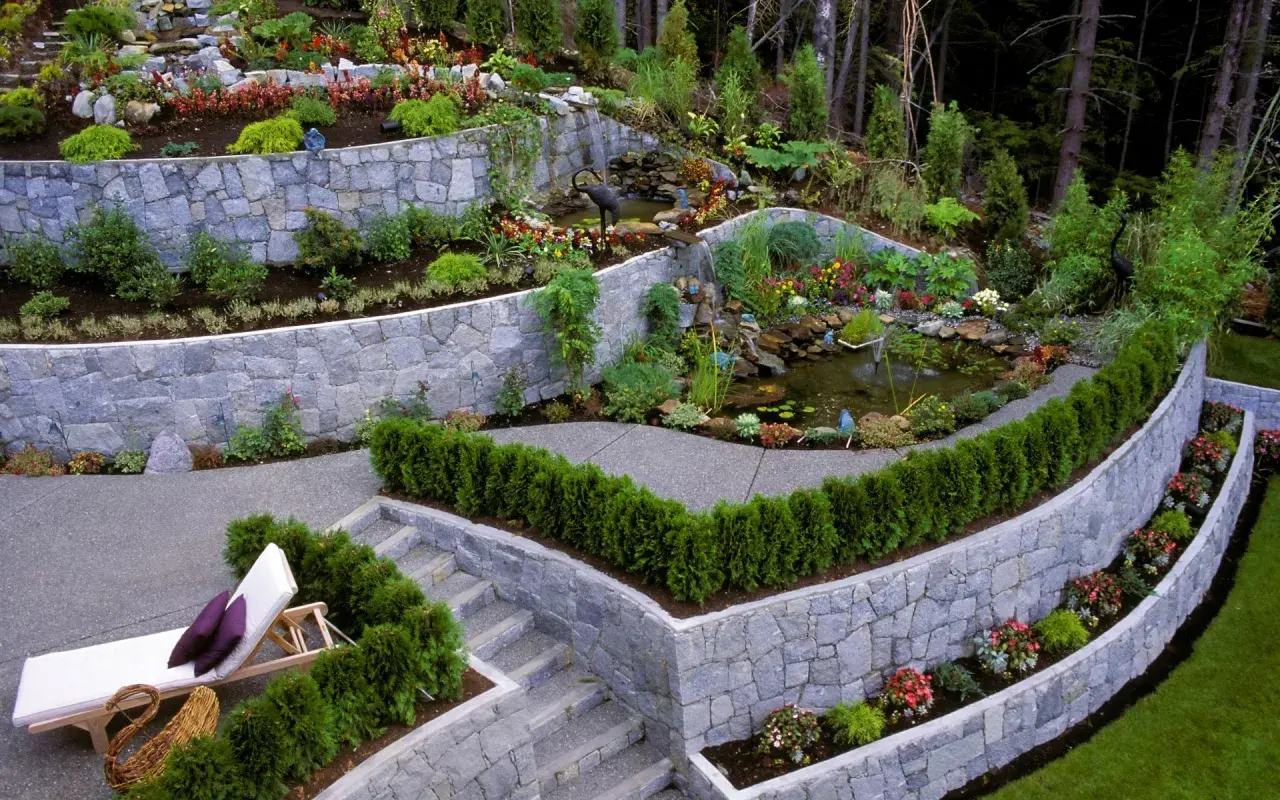 Giardino terrazzato con laghetto e cascata. Muri in pietra che creano livelli, illustrando la differenza tra muro di sostegno e muro di contenimento.
