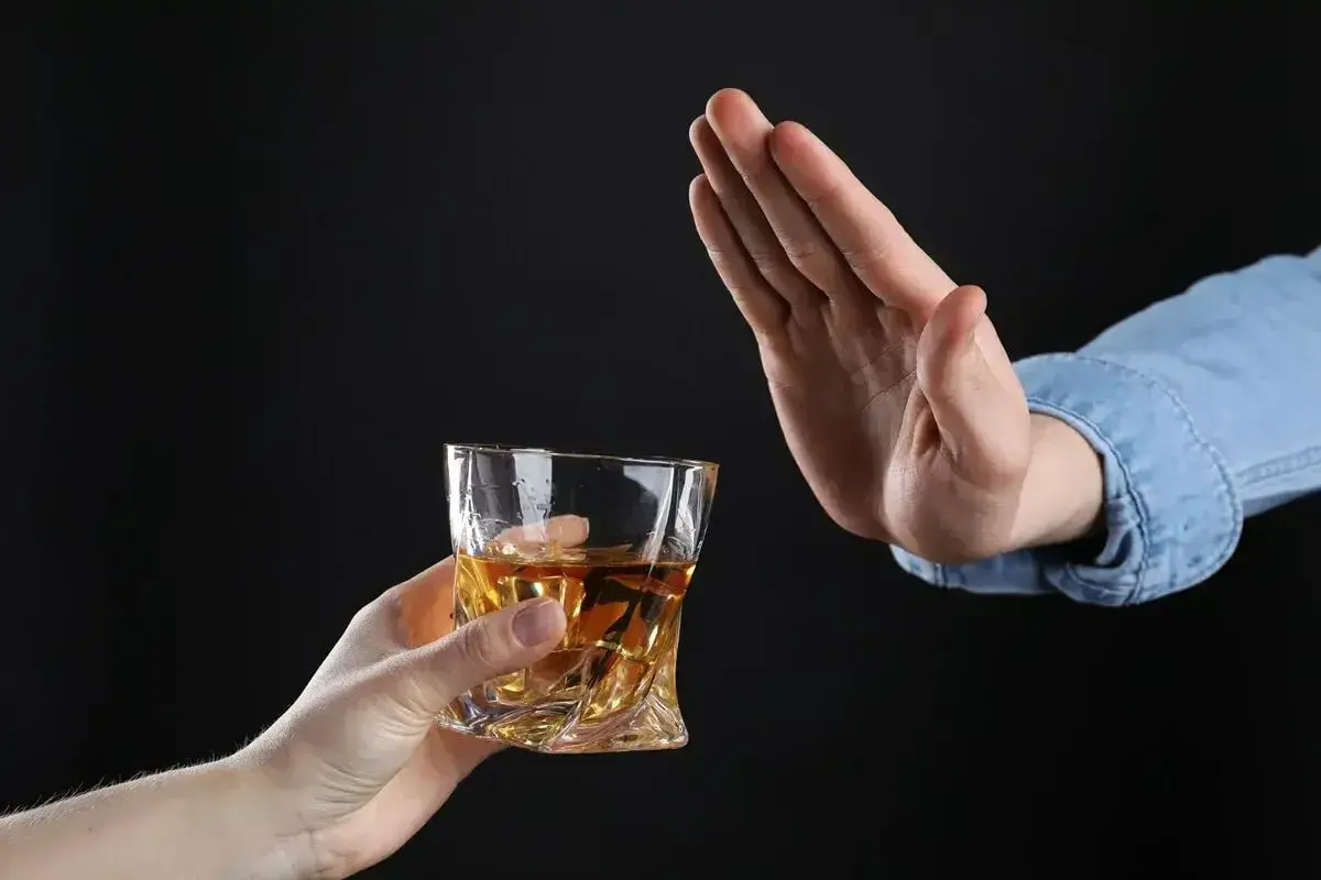 Ręka odrzuca szklankę z bursztynowym płynem. Czy dzień przed wizytą u dentysty można pić alkohol? Lepiej nie ryzykować.