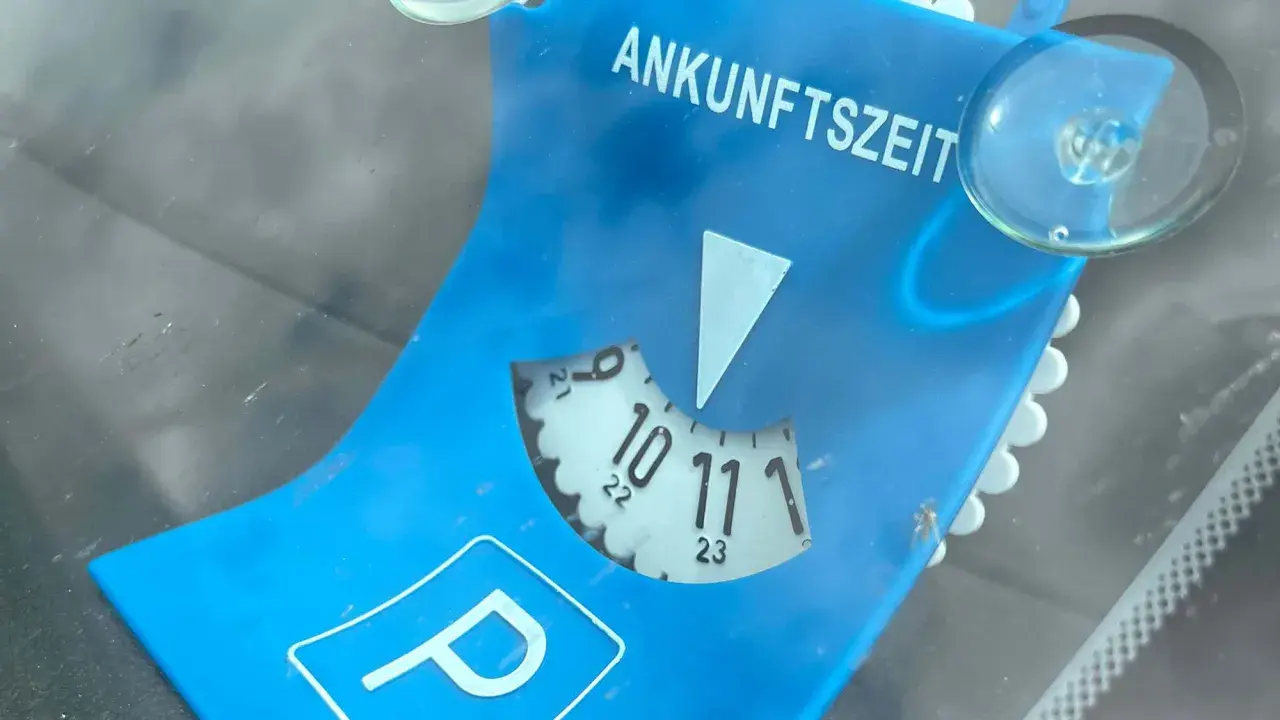 Blaue Parkscheibe mit der Aufschrift "ANKUNFTSZEIT". Die Scheibe ist auf 10:30 Uhr eingestellt, was 15 Minuten Parkzeit bedeutet.