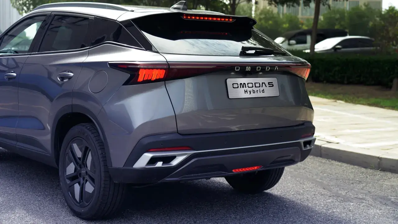 Szary OMODA 5 Hybrid z tyłu, z widocznym napisem "OMODA Hybrid" na klapie bagażnika. Nowoczesne światła LED i sportowy dyfuzor.