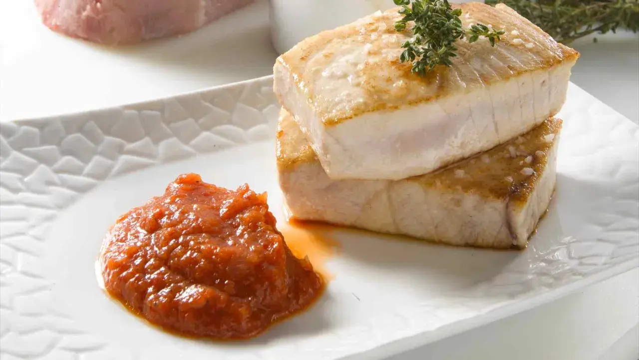 Dos jugosos medallones de atún a la plancha, con sal gruesa y romero, acompañados de una cucharada de salsa de tomate casera.