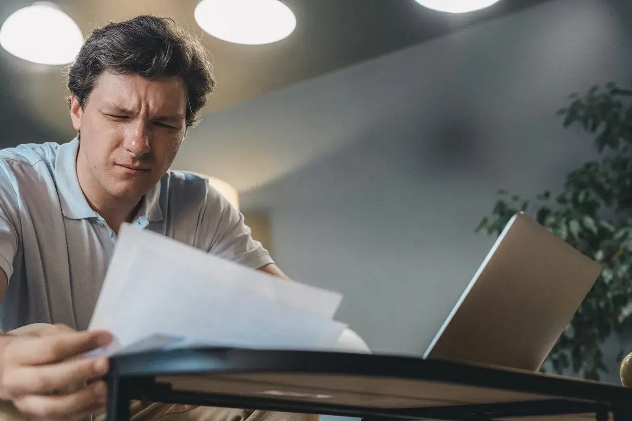 Mężczyzna zamyślony nad dokumentami, być może analizuje fakturę na osobę fizyczną. Obok laptop.