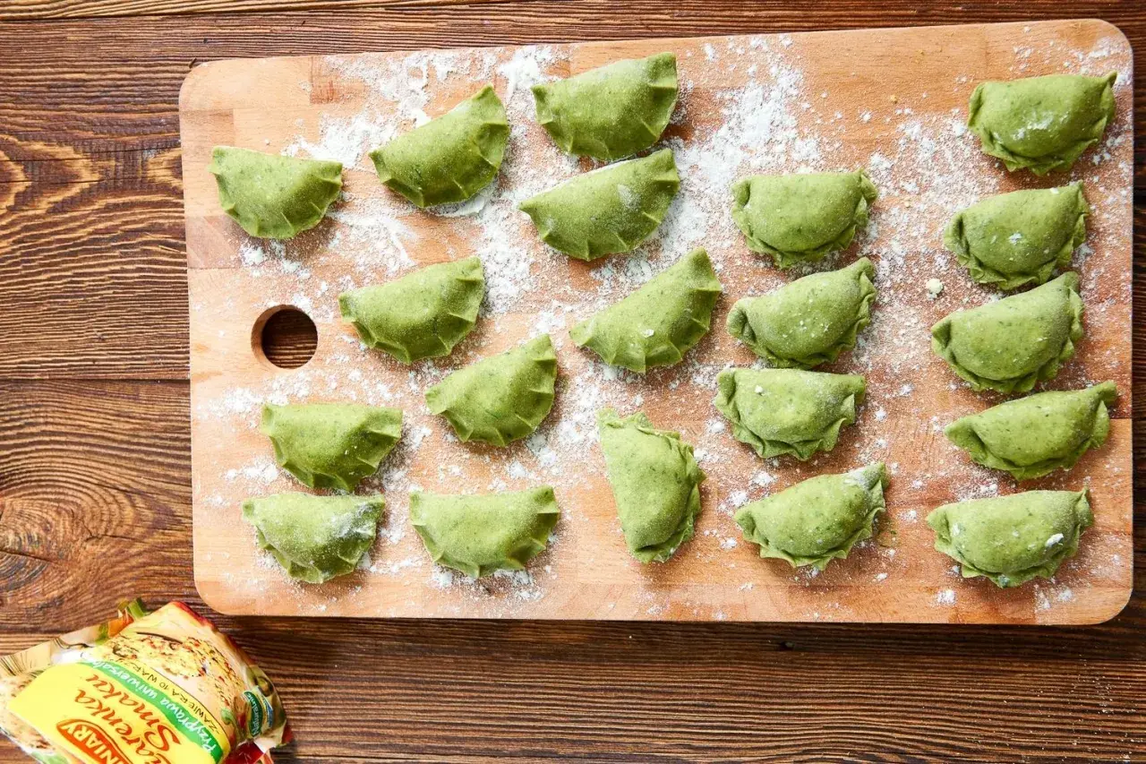 Zielone pierogi ze szpinakiem i serem feta ułożone na desce, posypane mąką.