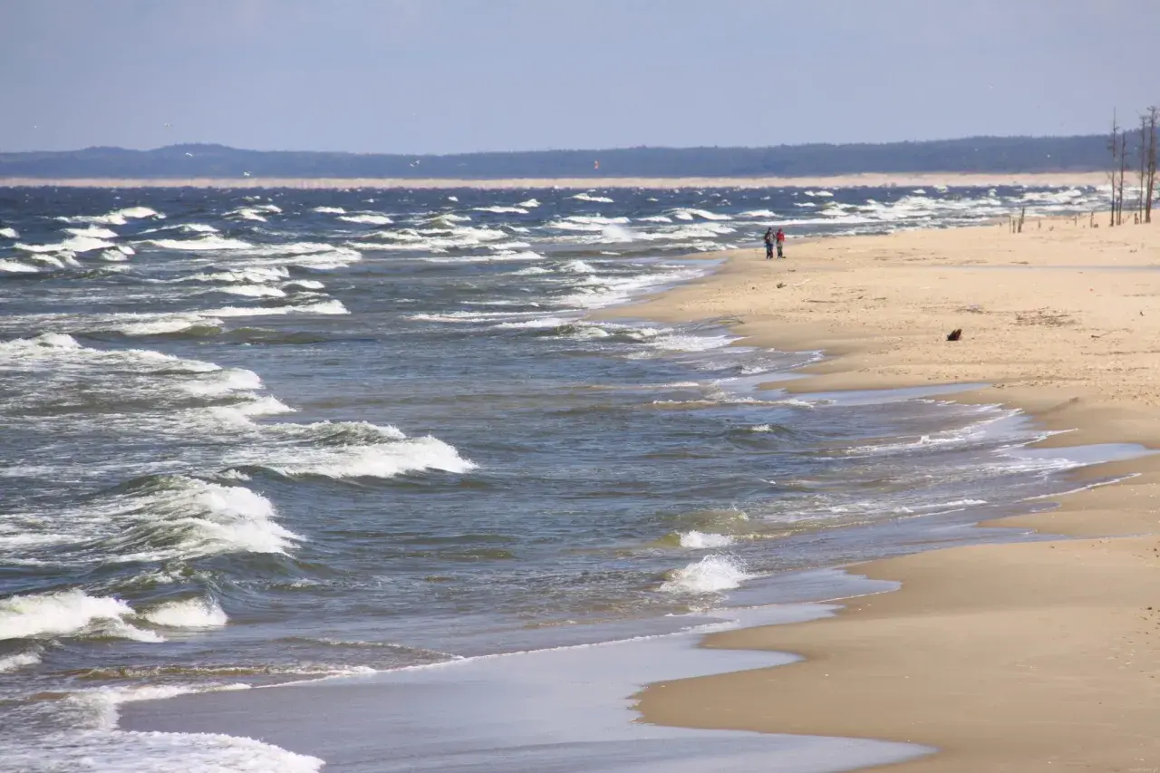 Plaża nad wzburzonym morzem, dwie osoby spacerują brzegiem.