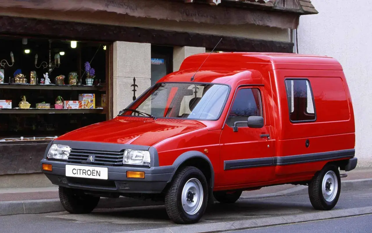 Czerwony Citroen C15, dostawczy klasyk, parkuje przed sklepem z pamiątkami.