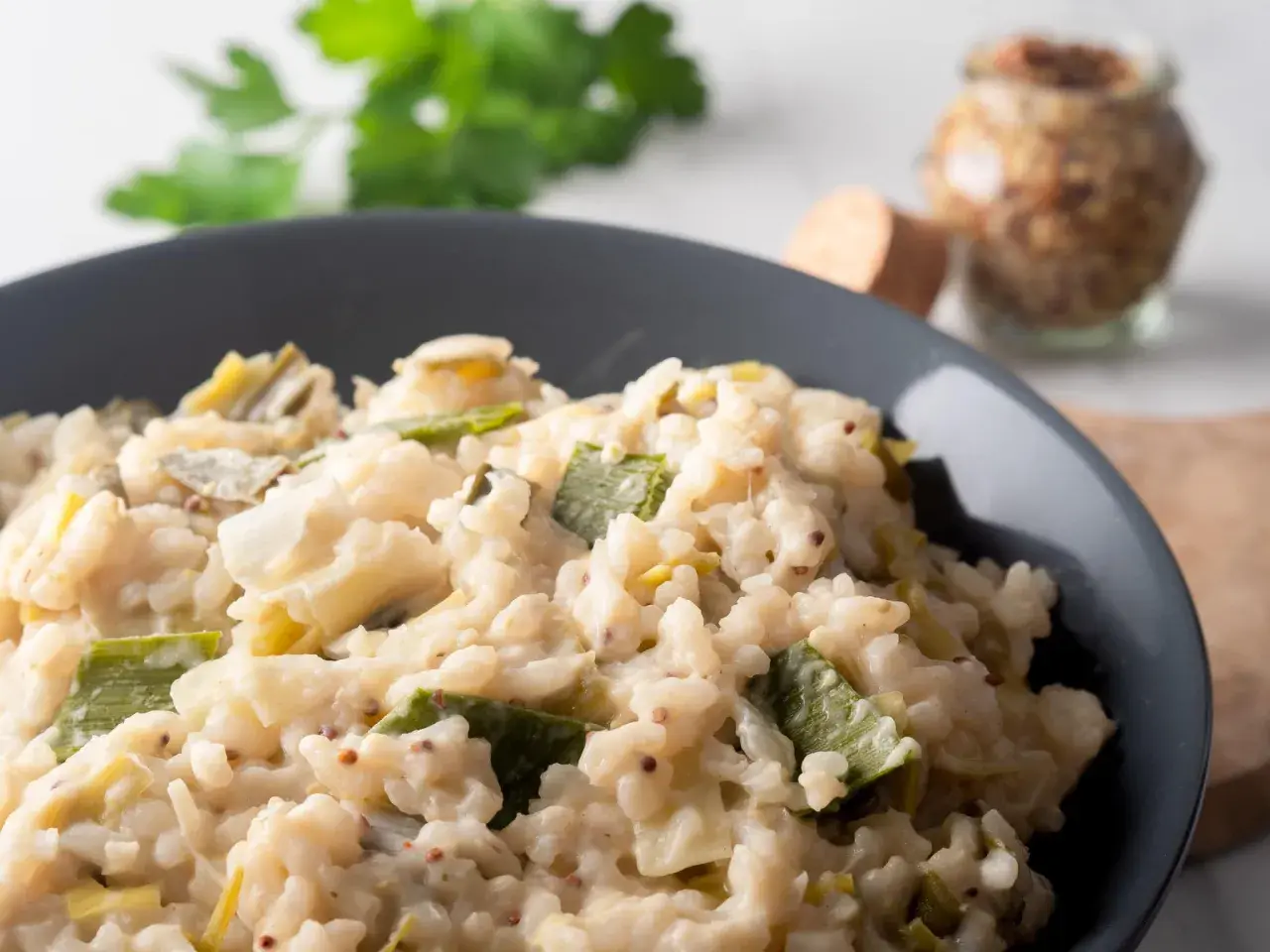 Un crémeux risotto poireaux, parsemé de grains de moutarde, servi dans un bol gris.