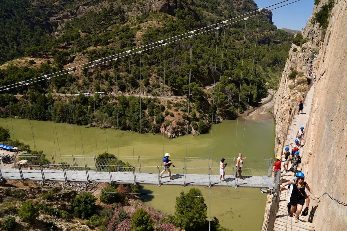 Visitantes caminan por la pasarela del Caminito del Rey, una impresionante ruta del rey entre acantilados y un río verde.