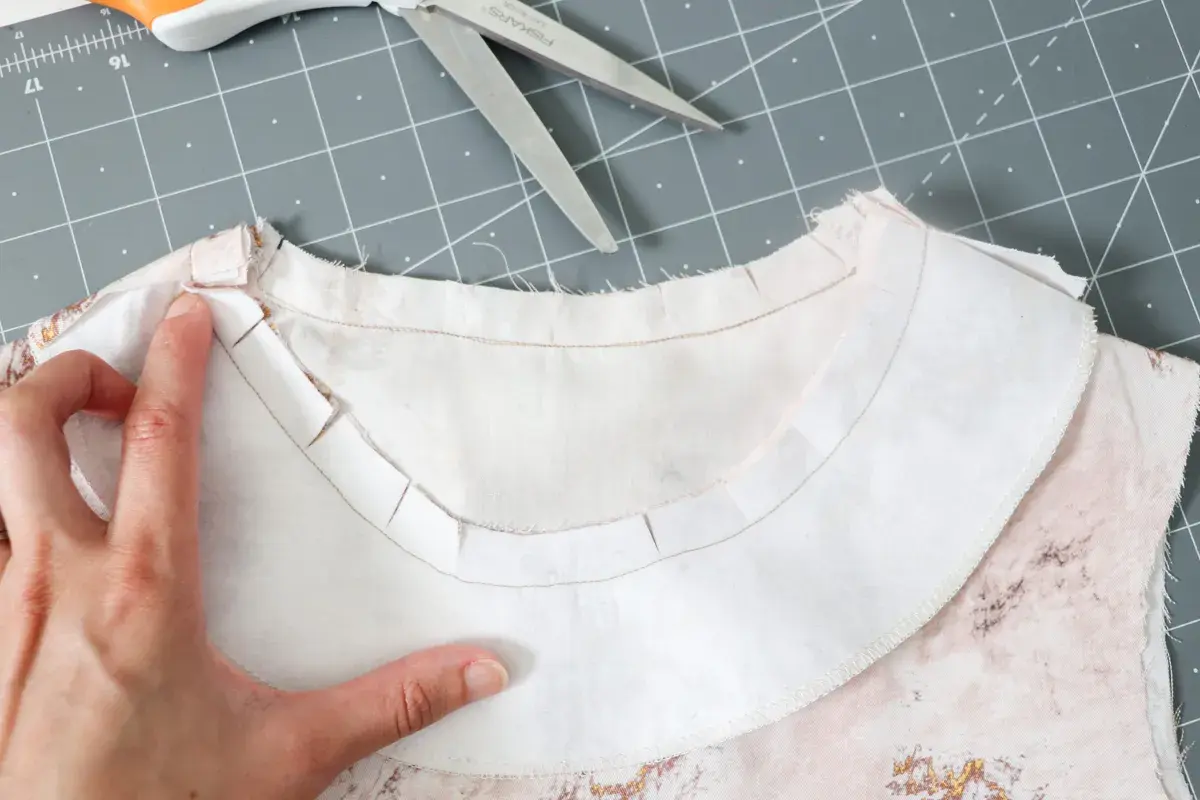 A hand guides the inner facing of a garment, showing the clipped seam allowance for a smooth neckline finish.
