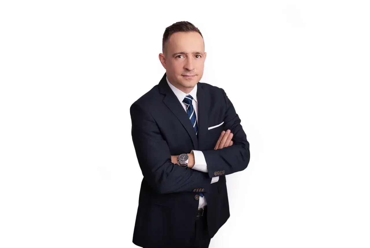 Mężczyzna w garniturze ze skrzyżowanymi rękami, na białym tle.