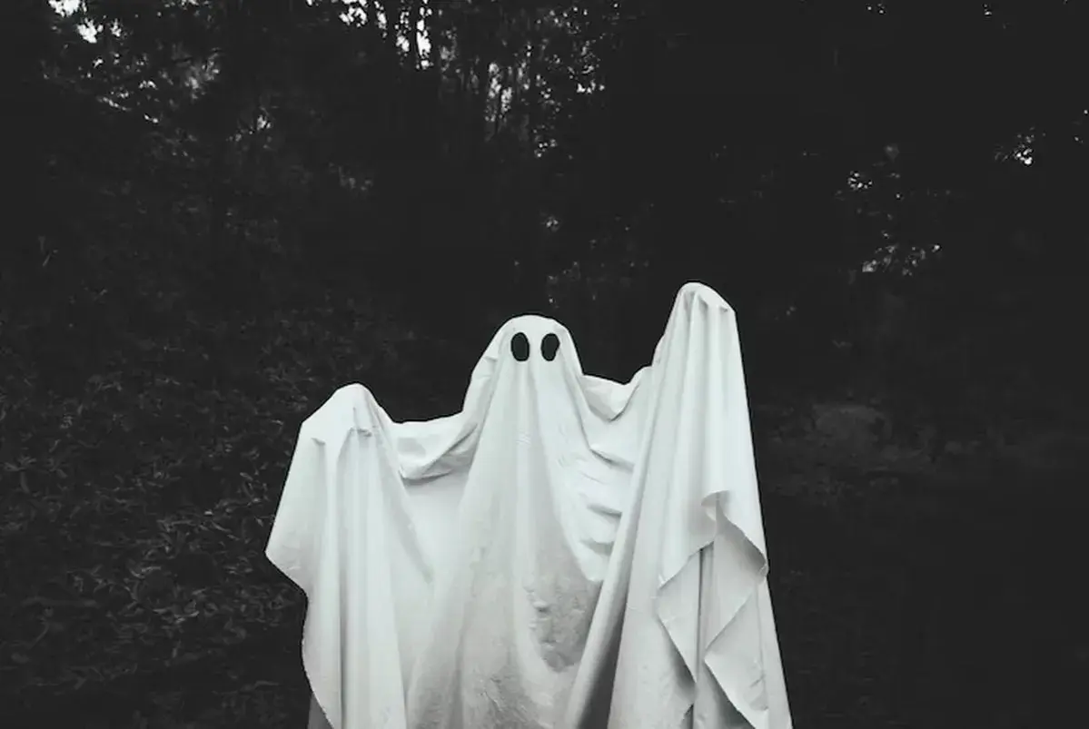 Figura fantasmal blanca con dos agujeros negros para ojos, en un bosque oscuro. ¿Qué significa soñar con fantasmas?