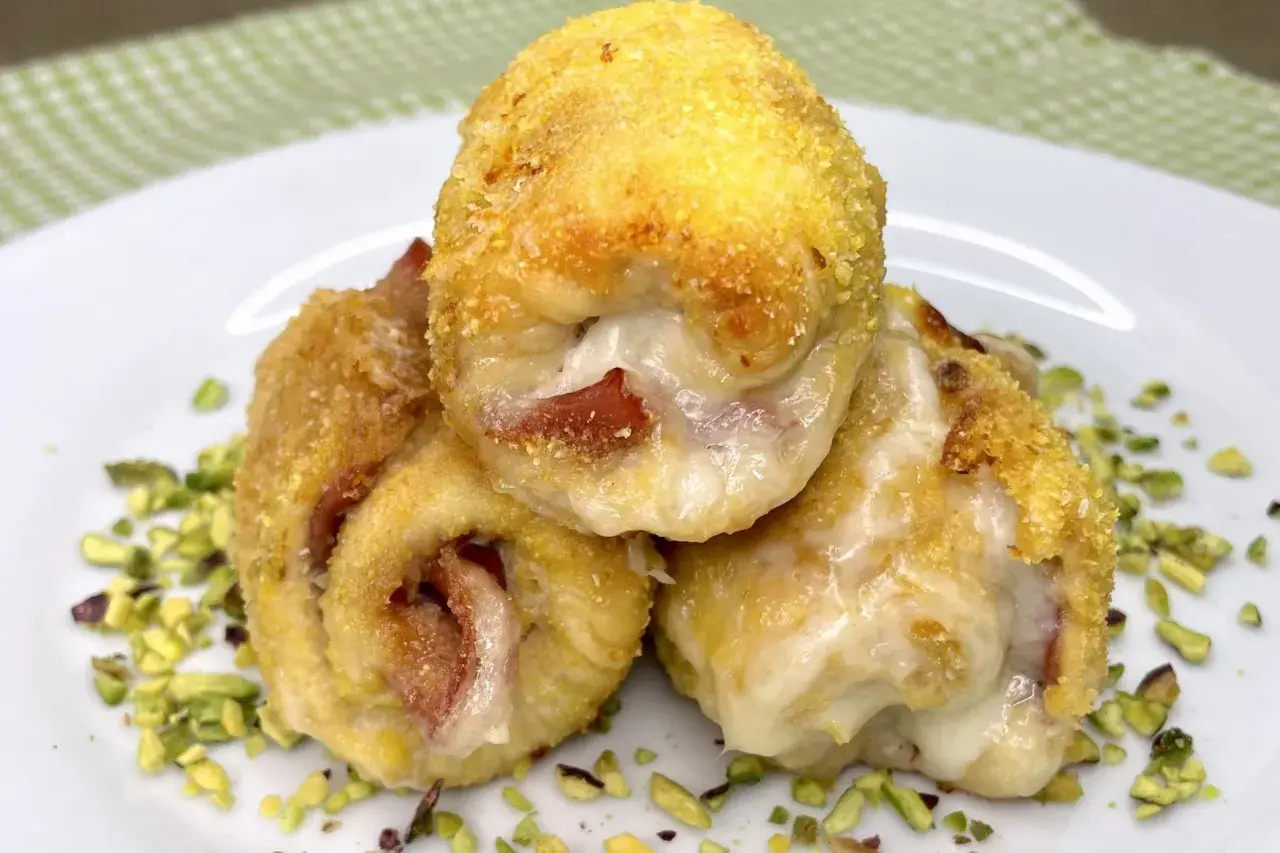 Tre involtini di pollo dorati e ripieni di formaggio filante e prosciutto, adagiati su un letto di pistacchi tritati.