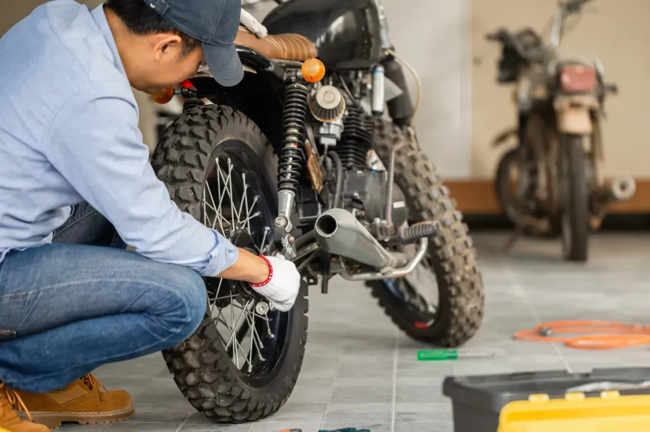 Mecánico revisa moto para su homologación. Herramientas y otra moto en el fondo.