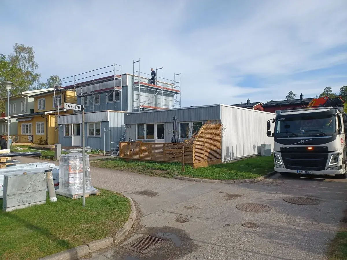 Byggnadsarbetare på ställningar vid hus som ska bygga till. En kranbil står parkerad.