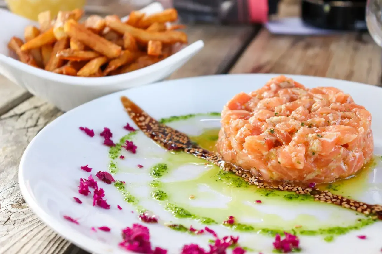 Tatar z łososia do sushi, podany z sosem i posypką z sezamu, obok miseczki frytek.