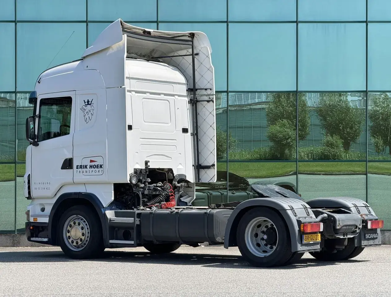 Biała Scania R420 z logo "Erik Hoek Transport" stoi przed nowoczesnym budynkiem z zielonymi oknami.