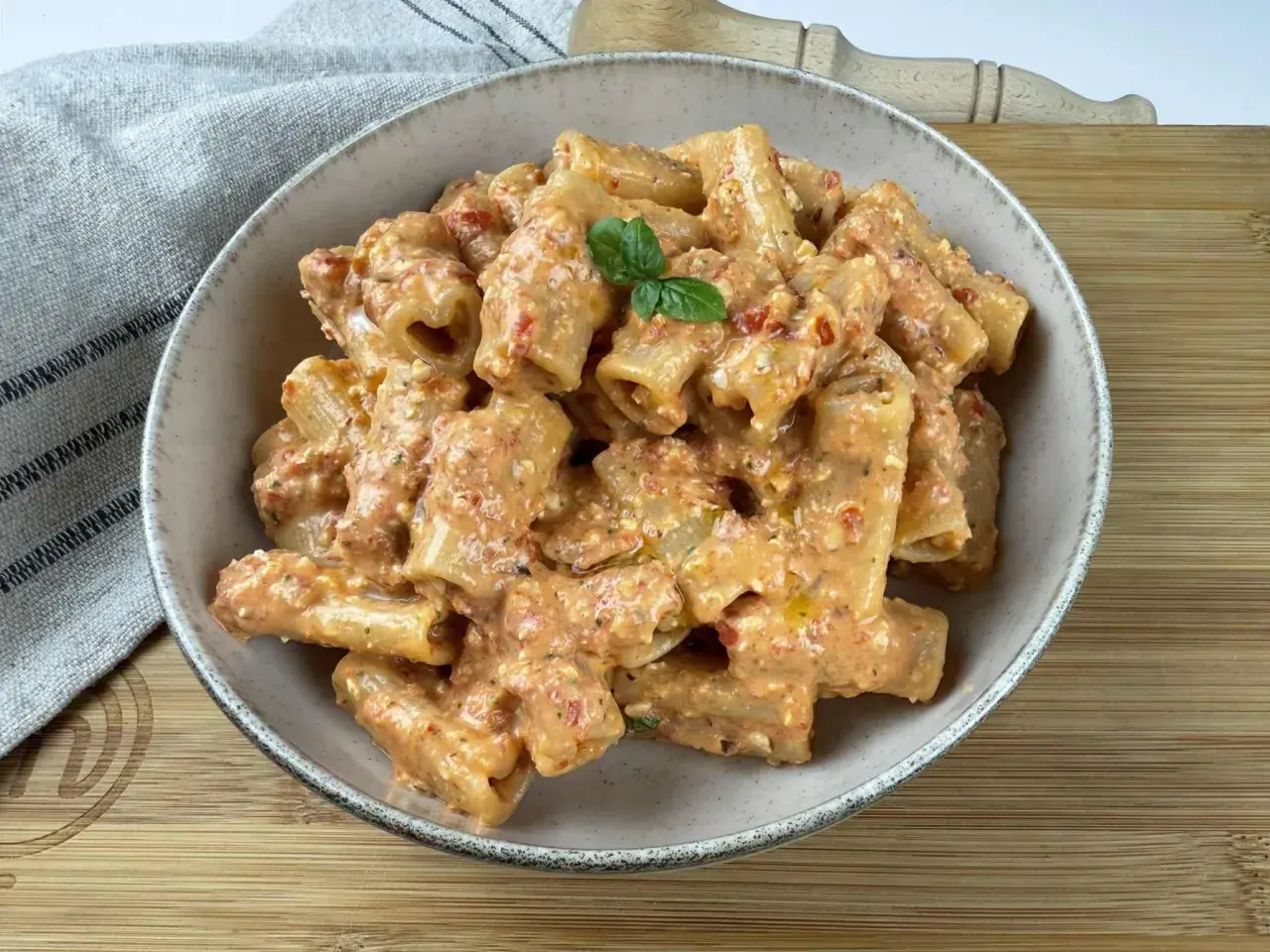 Rigatoni conditi con un cremoso pesto di pomodorini e ricotta, guarniti con basilico fresco.
