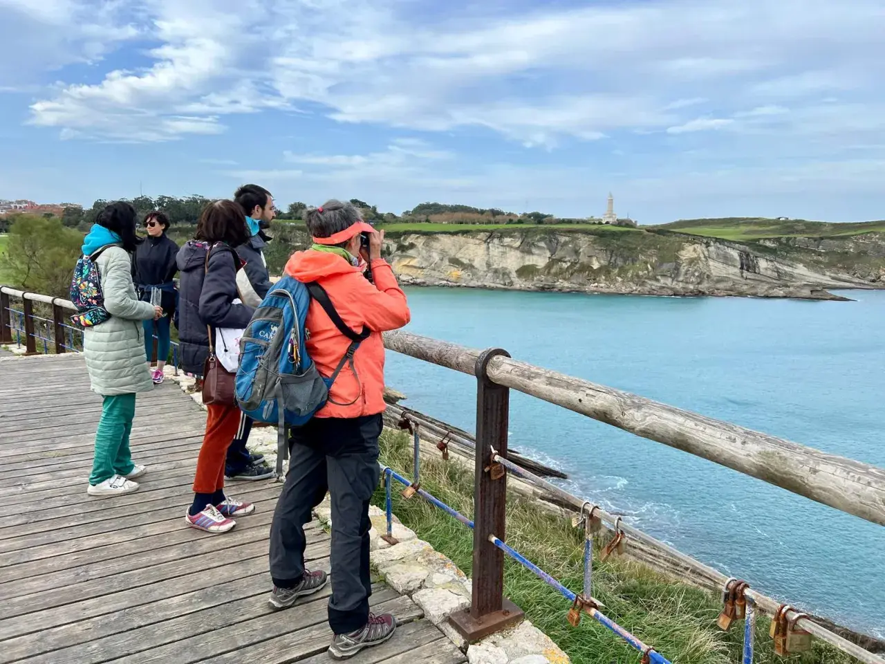 Disfrutando de las rutas por Santander, un grupo de amigos admira el faro y la costa desde un mirador de madera.