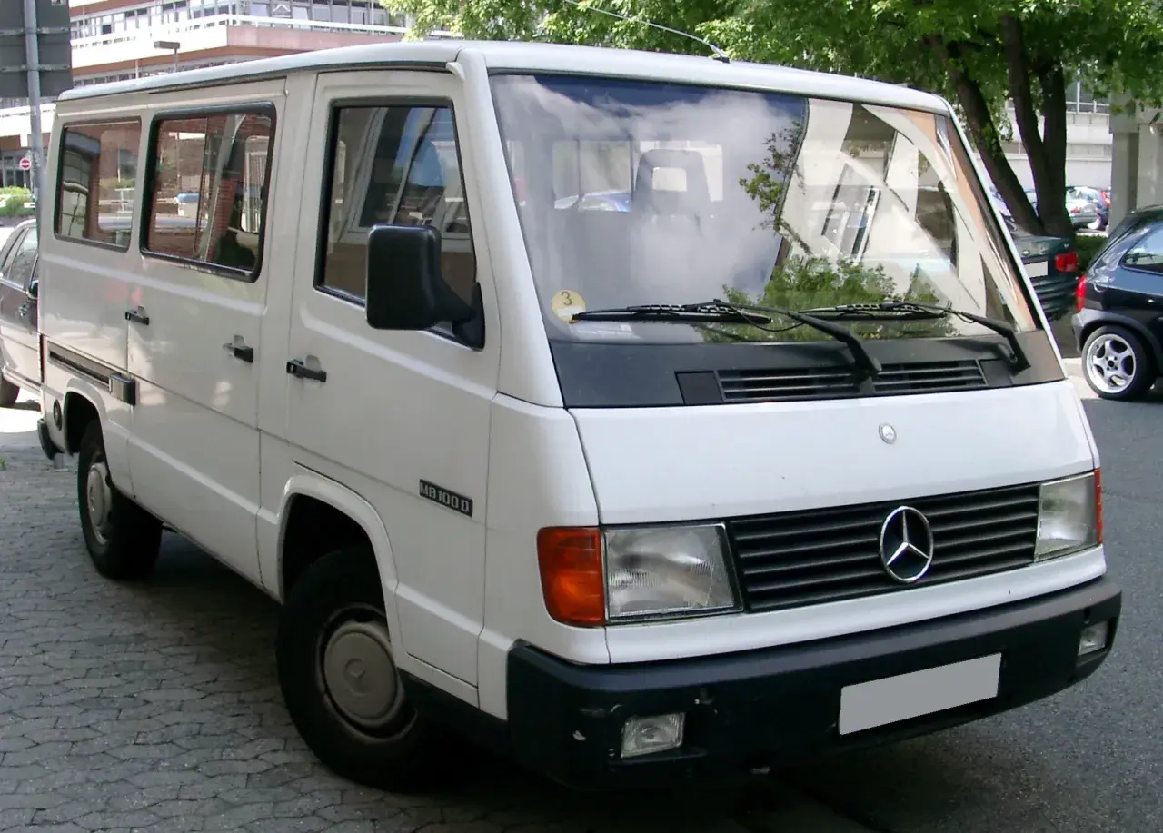 Biały Mercedes MB 100 D, klasyczny van, zaparkowany na ulicy.